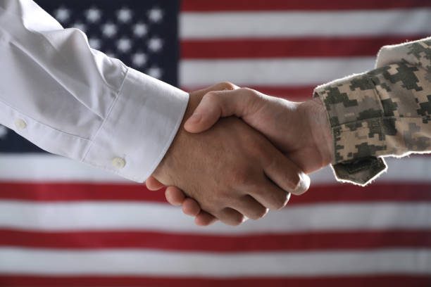 A handshake between a civilian and a soldier with an American flag backdrop.