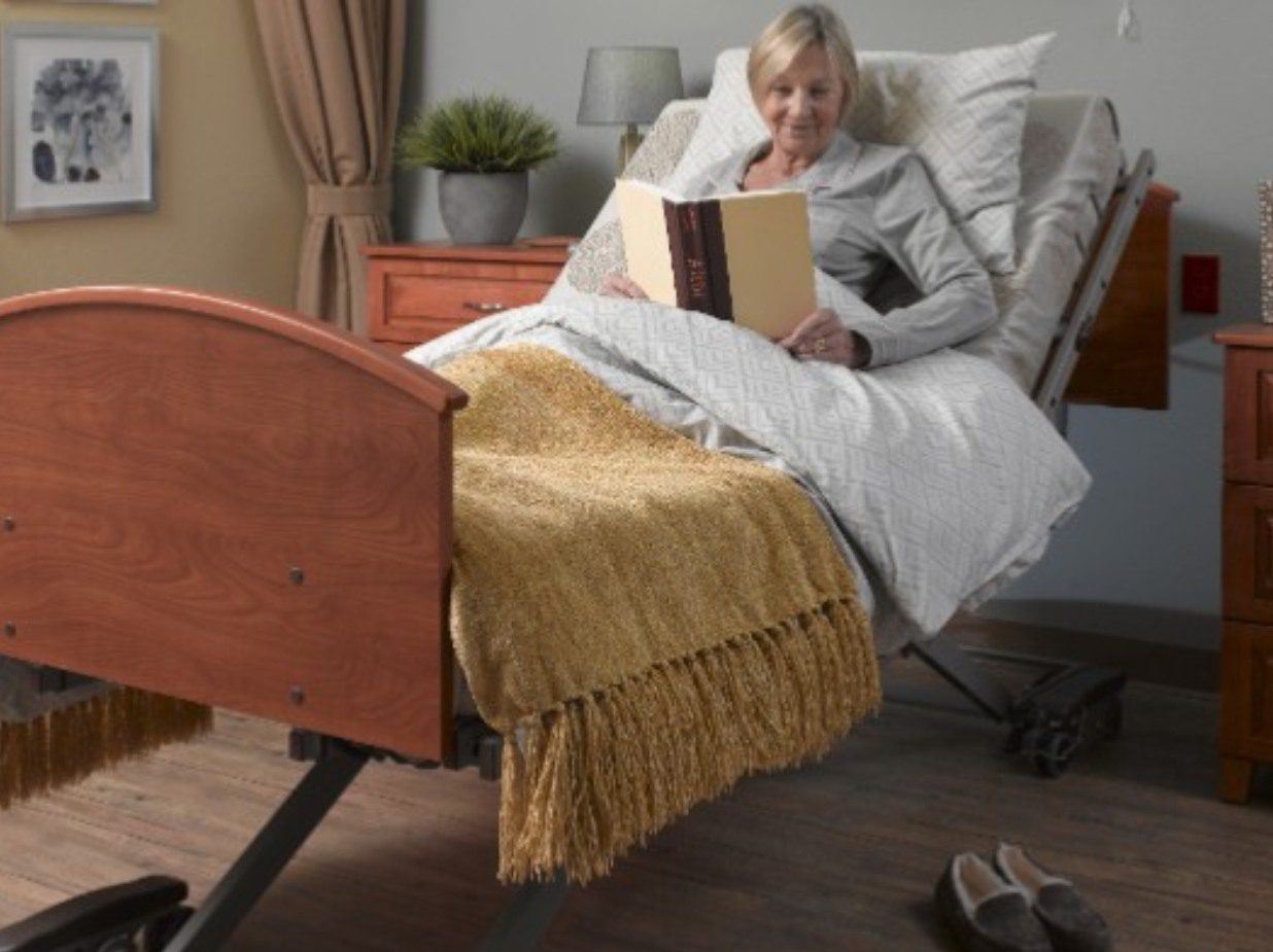 Elderly woman reading a book in a hospital bed with a cozy blanket.