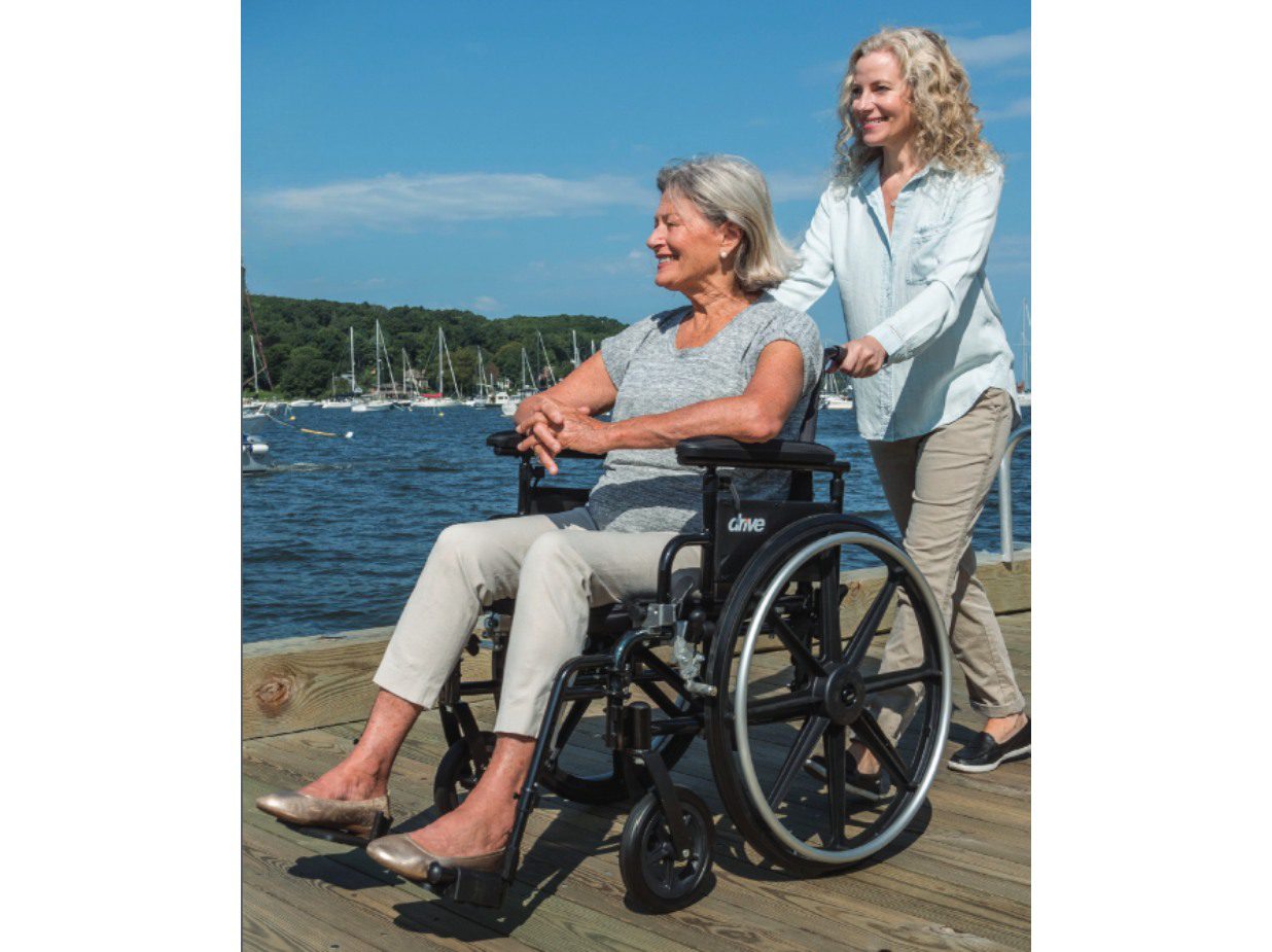 A woman pushing a smiling elderly woman in a wheelchair by the water.