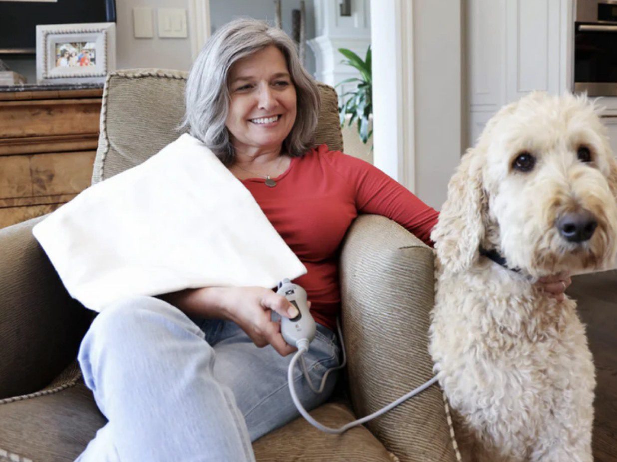 Woman relaxing on couch with a dog and a heating pad.